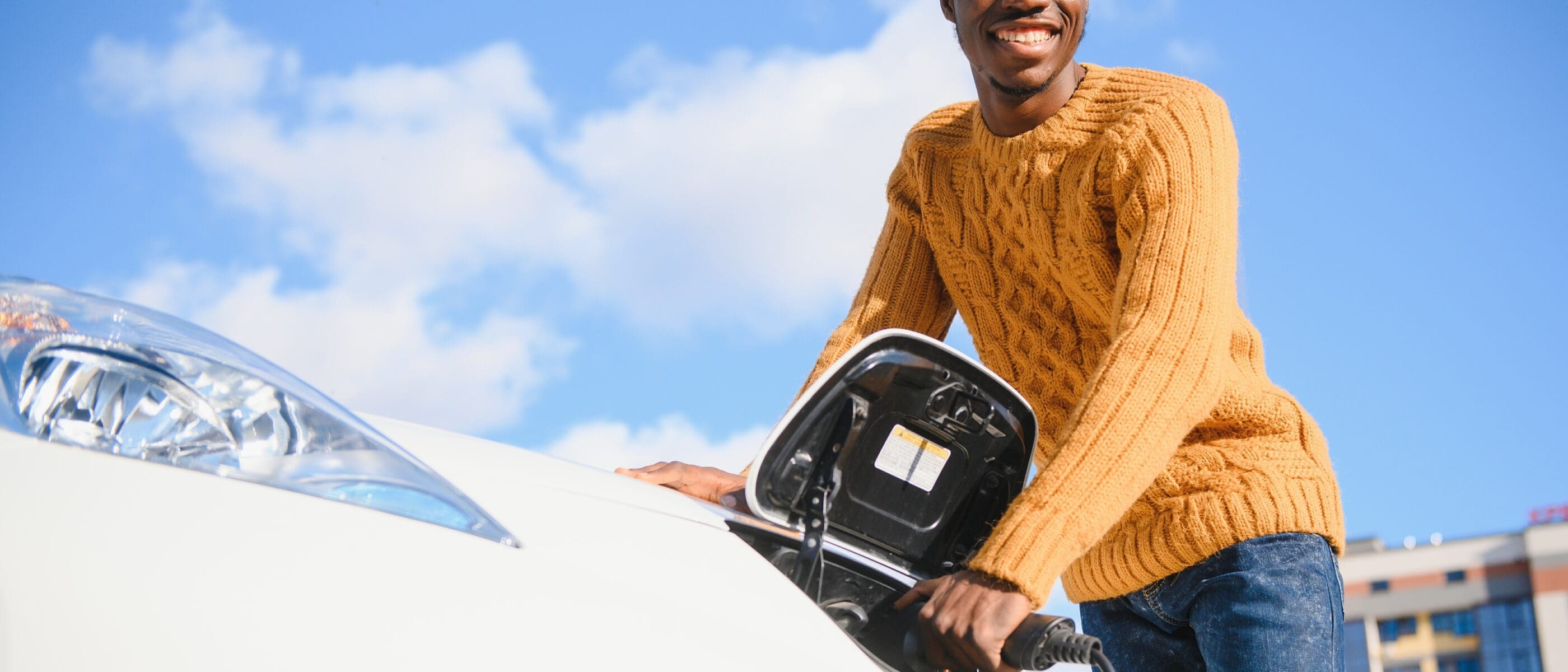 electric cars ev concept eco friendly fuel portrait young smiling black man recharging his modern luxury electric car scaled